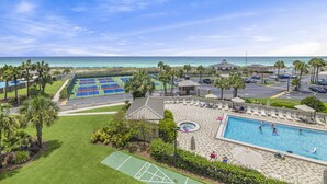 Zona de piscina con vistas a la playa, cancha de tenis y una pequeña pérgola.