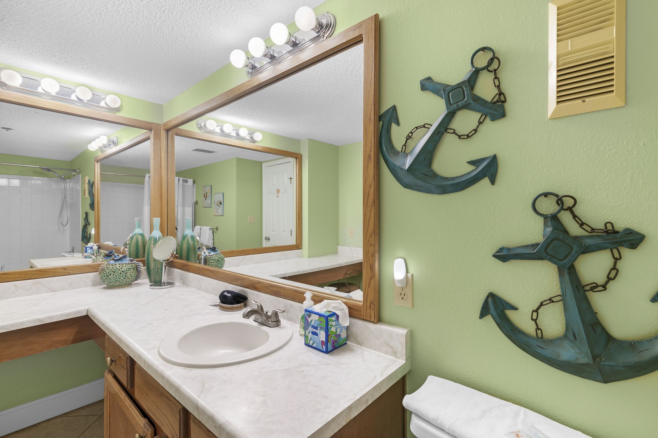 A bathroom with a large mirror, vanity, sink, and decorative anchors on the wall.