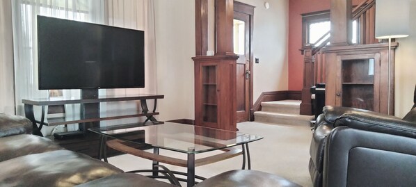 A living room with a flat-screen TV, leather sofas, a glass coffee table, and wooden furniture. - Park in the Garage and Walk to Mayo Clinic (Rochester)
