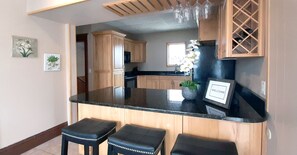 Una cocina con armarios de madera, encimera negra y dos taburetes negros.