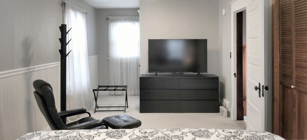 A bedroom with a bed, a chair, a TV on a stand, a dresser, and a door. - Park in the Garage and Walk to Mayo Clinic (Rochester)