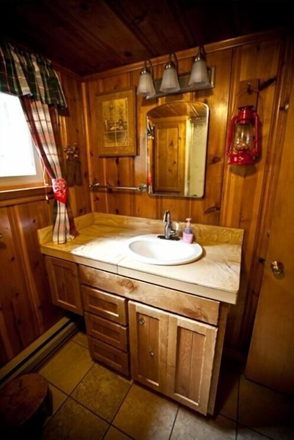 A wooden cabin-style bathroom with a sink, mirror, and cabinets.