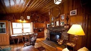 A cozy cabin interior with a wooden dining table, chairs, a fireplace, and a lamp. - Montgomery's Cozy Forest Retreat (Greer)