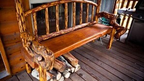 A rustic wooden bench with a curved backrest, placed on a wooden deck with logs underneath. - Montgomery's Cozy Forest Retreat (Greer)