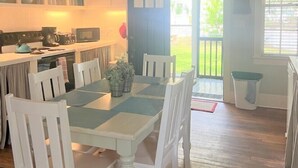 A kitchen with white cabinets, a dining table with chairs, a microwave, and a kettle. - Screened Inn c1925! Quiet North End Duplex! Screened porch. Beach Access! (Tybee Island)