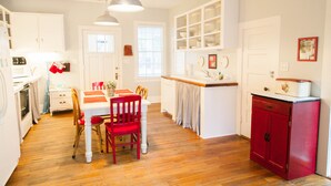 A kitchen with white cabinets, a red cabinet, a dining table with chairs, and a hanging light fixture. - Screened Inn c1925! Quiet North End Duplex! Screened porch. Beach Access! (Tybee Island)