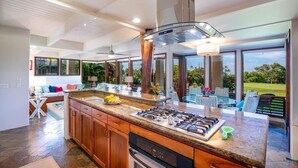 A modern kitchen with a large island, stainless steel appliances, and a view of the outdoors. - Sunlit Luxe Home ~ Ocean Vista + Sunsets + Full AC (Princeville)