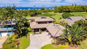 A large, two-story house with a spacious front yard, a garage, and a view of the ocean. - Sunlit Luxe Home ~ Ocean Vista + Sunsets + Full AC (Princeville)