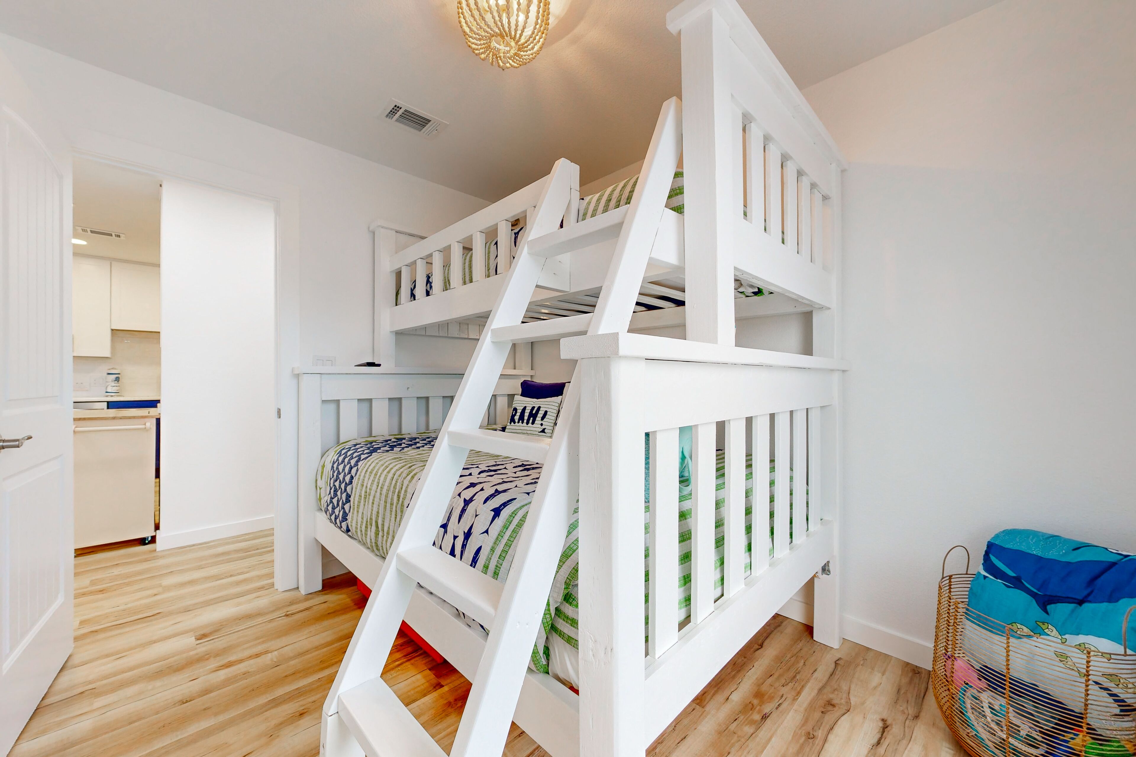 A room with a bunk bed, wooden flooring, and a kitchen visible through an open door.
