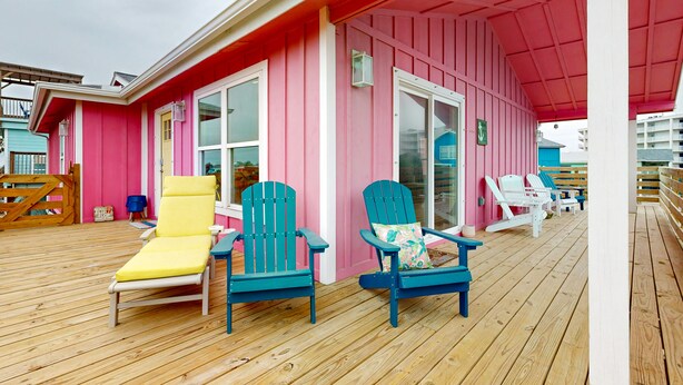 A pink building with a wooden deck, featuring several Adirondack chairs and a yellow lounge chair. - Ocean View from Back Porch, Boardwalk, Outdoor Shower (Port Aransas)