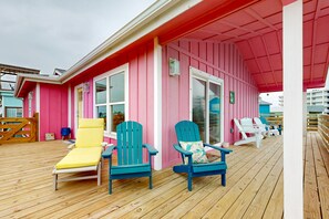 Ein rosafarbenes Gebäude mit einer Holzdielen-Terrasse, ausgestattet mit mehreren Adirondack-Stühlen und einem gelben Liegestuhl.