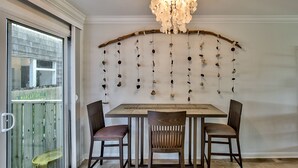 A dining area with a wooden table and two chairs, a chandelier, and a wall-mounted decoration of hanging objects.