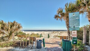 A beach entrance with a sign detailing beach rules, a no parking sign, and a trash can.