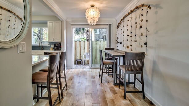 A kitchen with wooden flooring, a chandelier, and a dining area with chairs and a table.