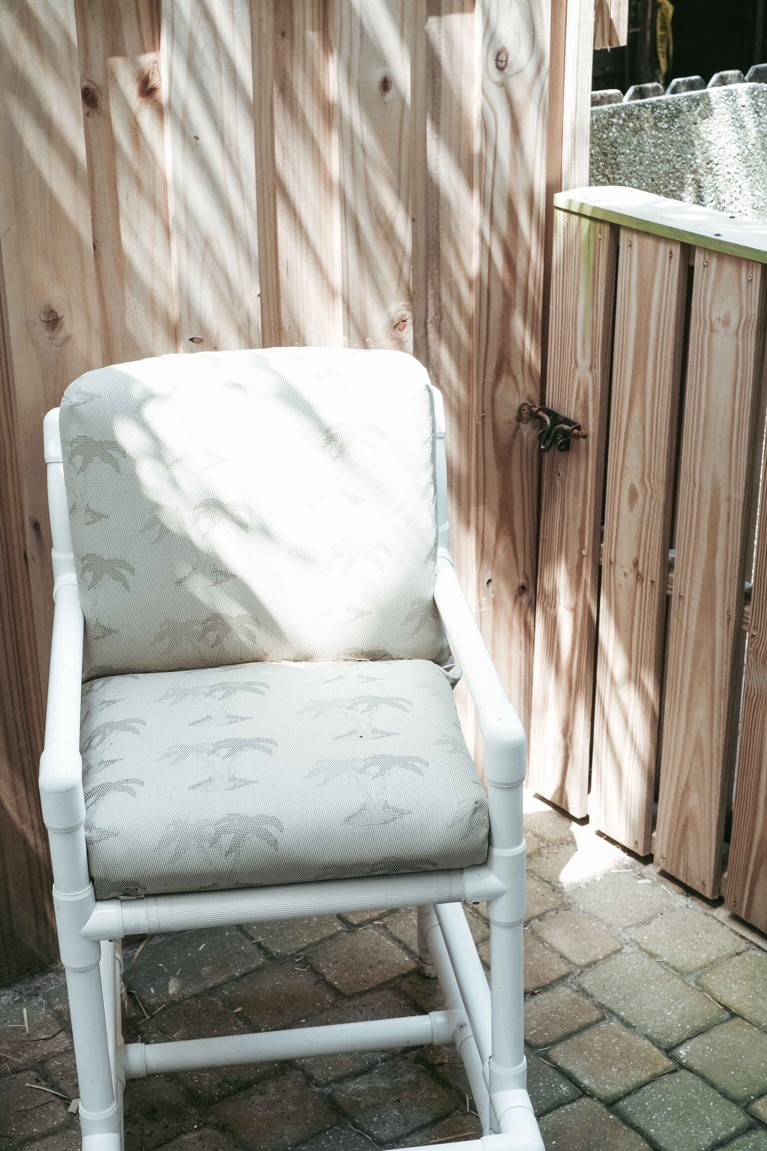 A white outdoor chair with a patterned cushion, positioned in front of a wooden fence.