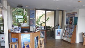 Una zona de recepción con un mostrador de madera, dos taburetes, un mapa y un cartel de un paisaje tropical.