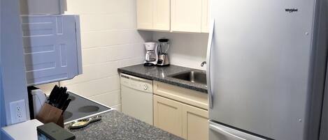 A compact kitchen with a built-in refrigerator, a coffee maker, and a dishwasher.