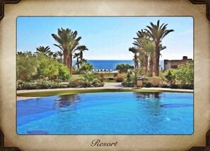 A resort with a swimming pool, palm trees, and a view of the ocean.