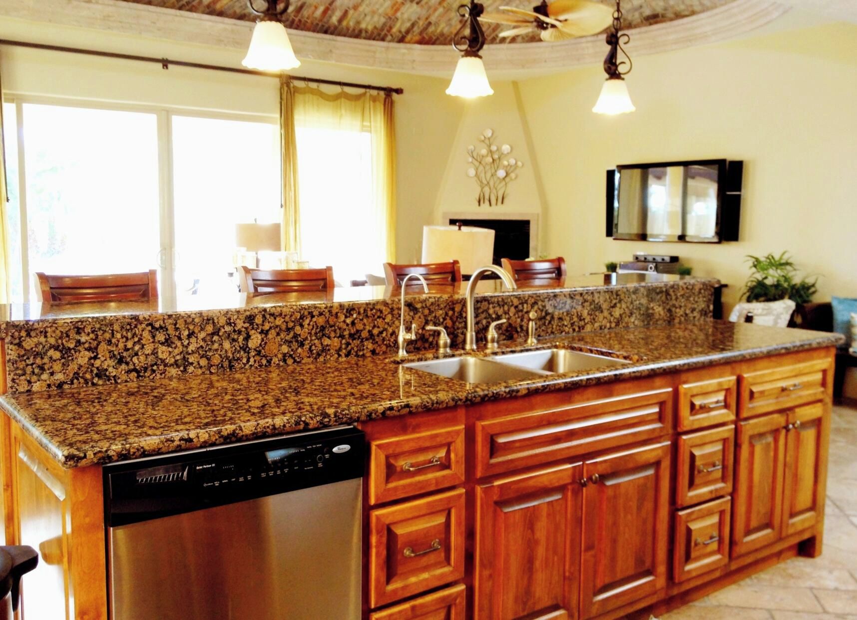 A kitchen with granite countertops, stainless steel appliances, wooden cabinets, and pendant lighting.