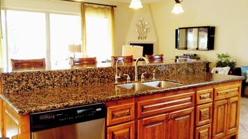 A kitchen with granite countertops, stainless steel appliances, wooden cabinets, and pendant lighting.