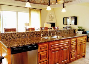 A kitchen with granite countertops, stainless steel appliances, wooden cabinets, and pendant lighting.