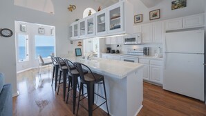 Una cocina con una isla grande, muebles blancos y vistas al exterior.