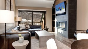 A modern living room with a leather sofa, a coffee table, a TV mounted on the wall, and a fireplace.
