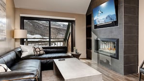 Uma sala de estar moderna com um sofá de couro, lareira e uma grande janela com vista para uma paisagem nevada.