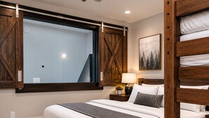 Quarto moderno com cama grande, cabeceira de madeira e vista pela janela.