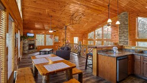 Interior de una cabaña de madera con comedor, cocina y chimenea.