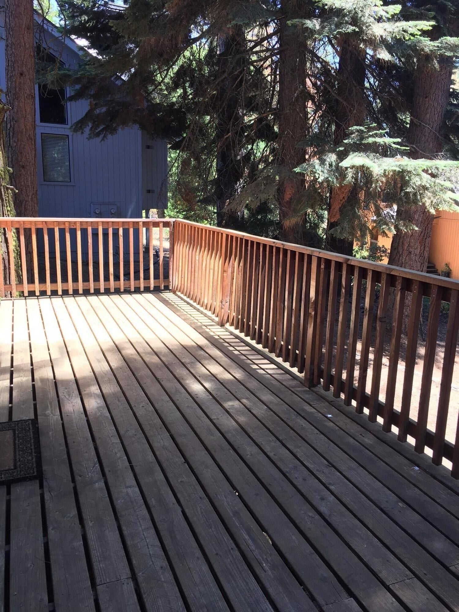 Una terraza de madera con barandilla, rodeada de árboles.