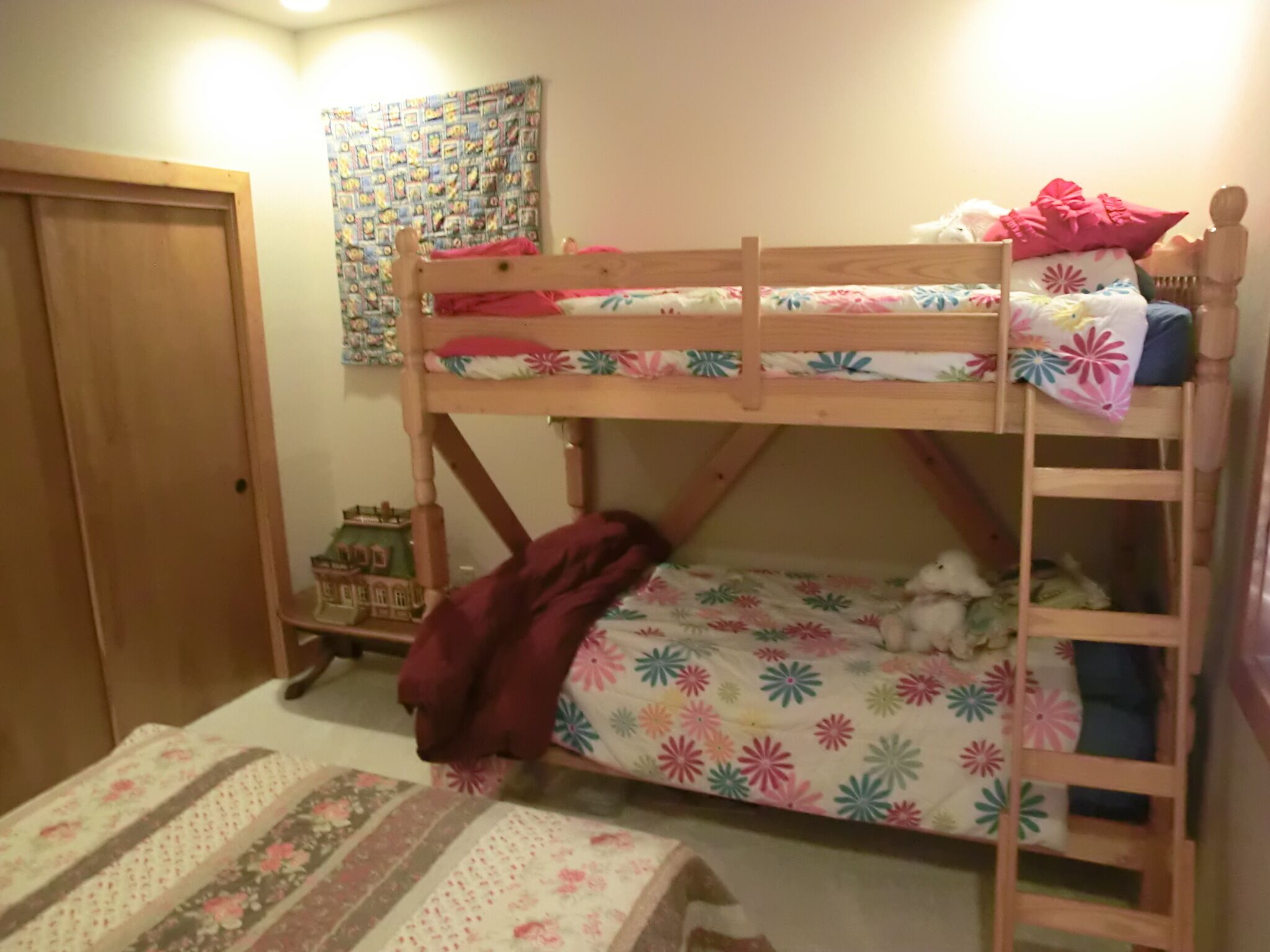 Una cama litera con ropa de cama floral, una pequeña casa de juguete de madera y una puerta.