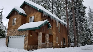 A log cabin with a stone foundation, a garage, and a porch with a stone railing.