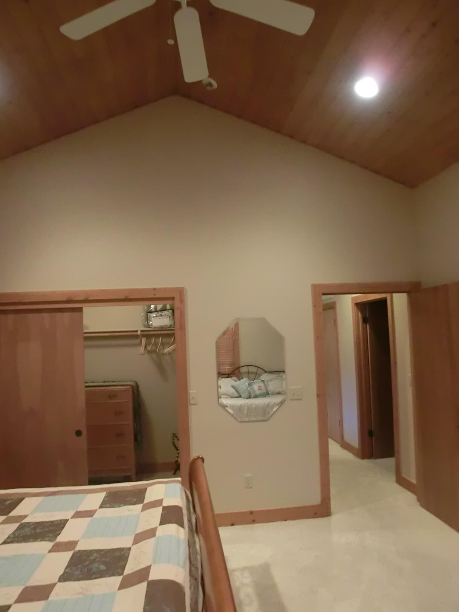 Un dormitorio con cama, ventilador de techo, espejo y armario.