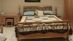 A bedroom with a wooden ceiling, a bed with a quilt, a nightstand, a desk, a chair, and a ceiling fan.