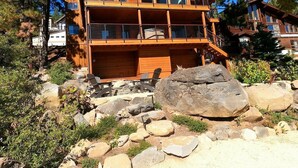Eine zweistöckige Holzhütte mit Balkon, umgeben von Felsen und Bäumen.