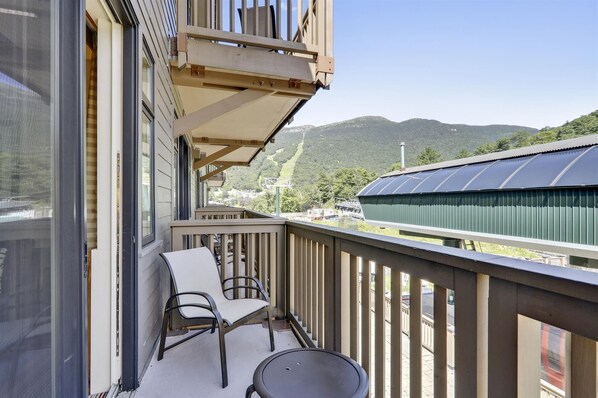 A balcony with a view of mountains, a chair, and a table.