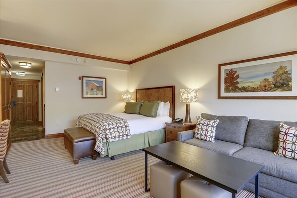 A hotel room with a bed, a sofa, a table, and a painting on the wall.