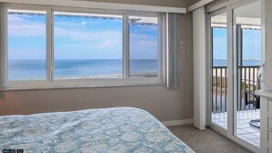 A bedroom with a large window overlooking a beach and a balcony with a view of the sea. - Sand Caper Beachfront Condo With Spectacular 7th Floor View of the Gulf! (Ft. Myers Beach)