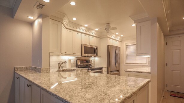 A modern kitchen with white cabinets, granite countertops, stainless steel appliances, and recessed ceiling lights. - Sand Caper Beachfront Condo With Spectacular 7th Floor View of the Gulf! (Ft. Myers Beach)