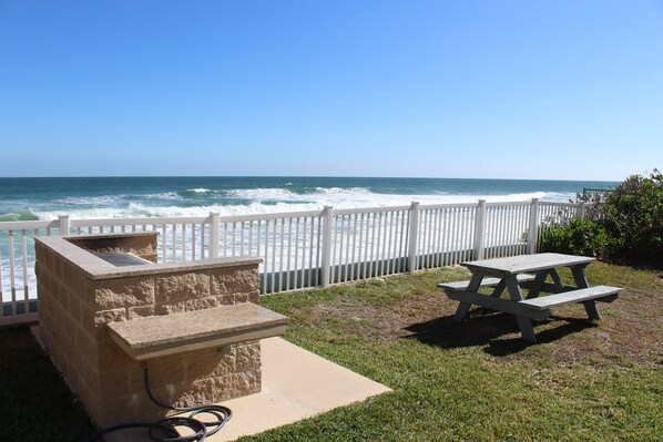 A patio with a stone barbecue and picnic table overlooking the ocean.