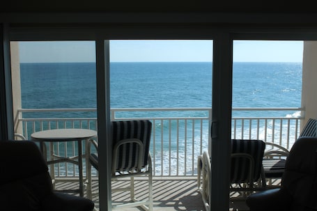A balcony with a view of the ocean, featuring two chairs and a small table.