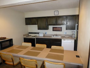 A compact kitchen with a dining table, chairs, a microwave, stove, toaster, sink, and cabinets.