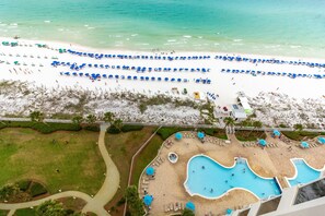 Un complexe hôtelier doté d’une grande piscine, de nombreux parasols et d’une plage de sable.