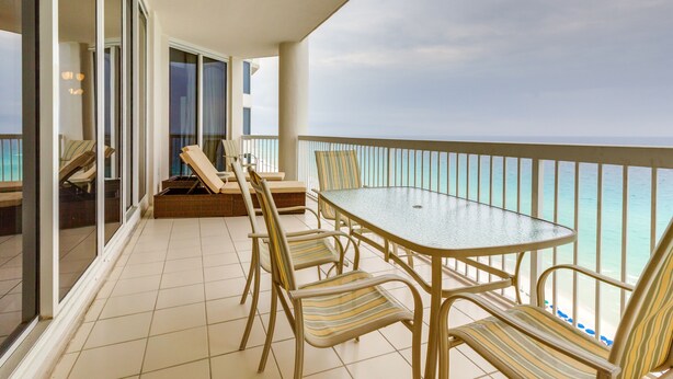 Un balcon avec une porte vitrée, une table ronde et des chaises à rayures.