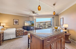 A hotel room with a bed, a desk, a television, a balcony with a view of a building, and a ceiling fan.