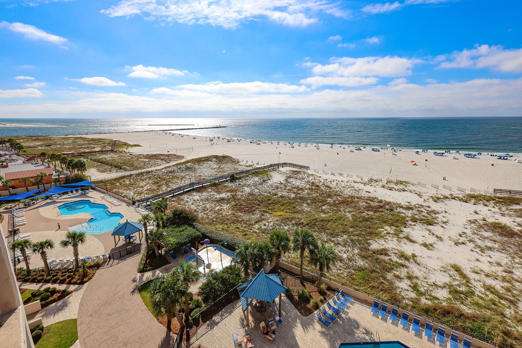 A beach resort with a swimming pool, lounge chairs, and a view of the beach and ocean.