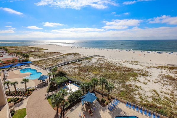 A beach resort with a swimming pool, lounge chairs, and a view of the beach and ocean.