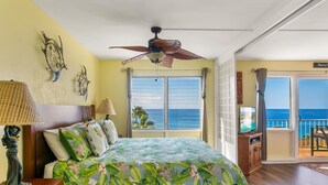 Ein Schlafzimmer mit Bett, Deckenventilator, Fernseher und einem Balkon mit Meerblick.