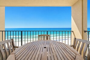 A wooden table and chairs on a balcony with a view of the beach and ocean.